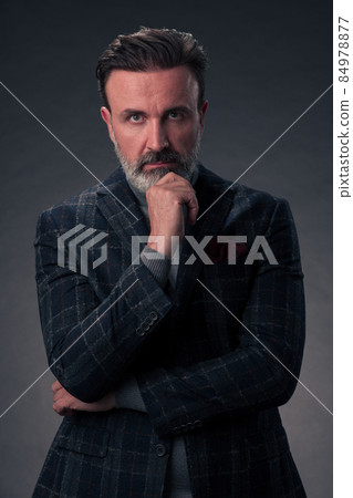 Portrait of a stylish elegant senior businessman with a beard and casual business clothes in photo studio isolated on dark background gesturing with hands 84978877