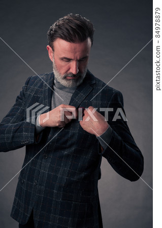 Portrait of a stylish elegant senior businessman with a beard and casual business clothes in photo studio isolated on dark background gesturing with hands 84978879