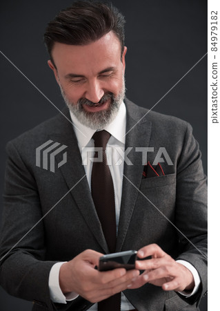 Portrait of adult businessman wearing trendy suit and sitting in modern studio on stylish chair against the black background 84979182