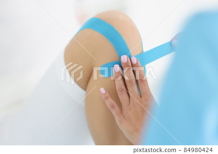 Physiotherapist put kinesiology blue tape on patient knee Physiotherapist put kinesiology blue tape on patient knee 84980424