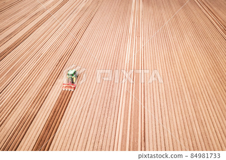 Lonely tractor on agricultural field with rows of plowed soil 84981733