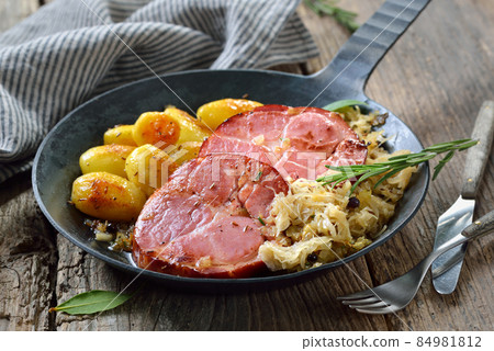 German food - Smoked neck of pork with sauerkraut and fried baby potatoes served in a frying pan 84981812