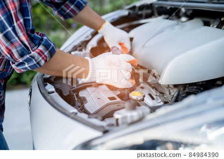 Asian auto mechanic check for repair under the hood of broken down car on the side of the road. 84984390