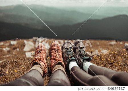 Couples legs together on the rock on top of the hill with mountain background. Hikers boots. Summer time, explore together 84986187