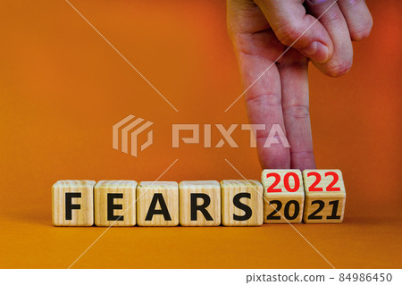 2022 fears new year symbol. Businessman turns wooden cubes and changes words 'Fears 2021' to 'Fears 2022'. Beautiful orange background, copy space. Business, 2022 fears new year concept. 2022 fears new year symbol. Businessman turns wooden cubes and changes words 'Fears 2021' to 'Fears 2022'. Beautiful orange background, copy space. Business, 2022 fears new year concept. 84986450