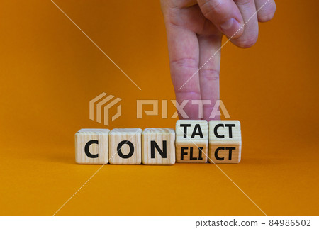 Conflict or contact symbol. Businessman turns wooden cubes and changes the word 'conflict' to 'contact'. Beautiful orange table, orange background, copy space. Business, conflict or contact concept. 84986502