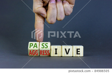 Passive or aggressive symbol. Businessman turns wooden cubes and changes the word passive to aggressive. Beautiful grey background, copy space. Business, psychological passive aggressive concept. Passive or aggressive symbol. Businessman turns wooden cubes and changes the word passive to aggressive. Beautiful grey background, copy space. Business, psychological passive aggressive concept. 84986505