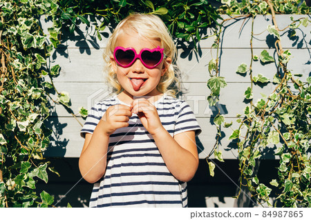 A funny little girl in sunglasses shows her tongue. A funny little girl in sunglasses shows her tongue. 84987865