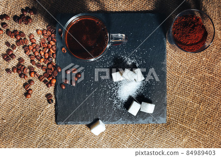 black coffee in a transparent glass Cup on background of burlap. coffee beans and ground coffee. view top black coffee in a transparent glass Cup on background of burlap. coffee beans and ground coffee. view top 84989403