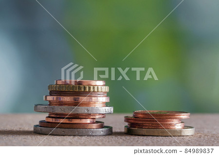 Two piles of coins different size and color stacked on each other on colorful blue and green copy space background. Money saving and financial risk concept. 84989837