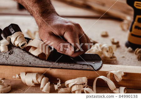 Carpenter's hands planing a plank of wood with a hand plane Carpenter's hands planing a plank of wood with a hand plane 84990138