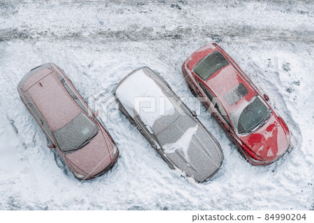 Top aerial view of apartment office building parking lot with many cars covered by snow stucked after heavy blizzard snowfall winter day. Snowdrifts and freezed vehicles. Extreme weather conditions 84990204