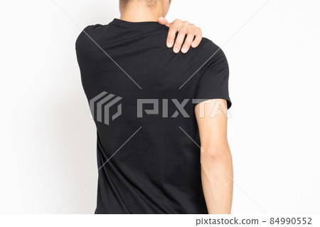 穿著黑色 T 恤的年輕人站在白色背景前,摸著他的肩膀 穿著黑色 T 恤的年輕人站在白色背景前,摸著他的肩膀 84990552