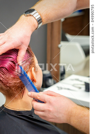 Hands of hairdresser combing hair making short pink hairstyle for a young caucasian woman in a beauty salon. Hands of hairdresser combing hair making short pink hairstyle for a young caucasian woman in a beauty salon. 84990795