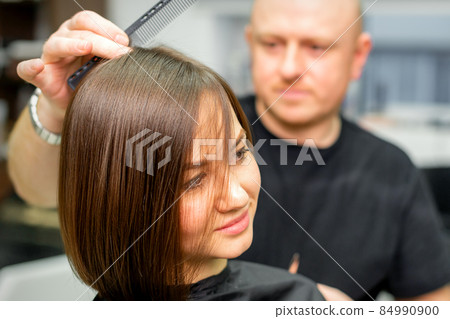 Young caucasian brunette woman having her hairstyling by a male hairdresser at a parlor. Young caucasian brunette woman having her hairstyling by a male hairdresser at a parlor. 84990900