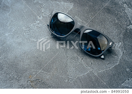 Dark male sunglasses on grey concrete surface Dark male sunglasses on grey concrete surface 84991050