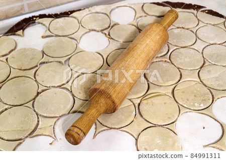 Rolling pin with dough on kitchen table. Preparing dough round tortillas for cookings to be baked. Rolling pin with dough on kitchen table. Preparing dough round tortillas for cookings to be baked. 84991311