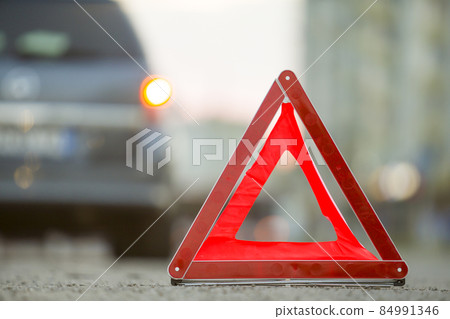 Red emergency triangle stop sign and broken car on a city street. Red emergency triangle stop sign and broken car on a city street. 84991346