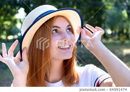 Portrait of happy smiling girl with red hair and in yellow hat outdoors in summer park. Portrait of happy smiling girl with red hair and in yellow hat outdoors in summer park. 84991474