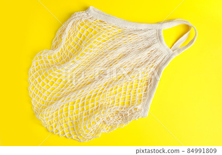 Eco-friendly mesh bag on a yellow background. Recyclable organic cotton bag. Sustainable lifestyle and shopping. Eco-friendly mesh bag on a yellow background. Recyclable organic cotton bag. Sustainable lifestyle and shopping. 84991809