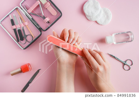 Woman does a manicure at home. Hands with a nail file on a pink background. 84991836