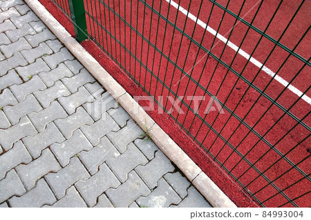 Close-up of white marking lines of outdoor basketball court fenced with protective metal fence. 84993004
