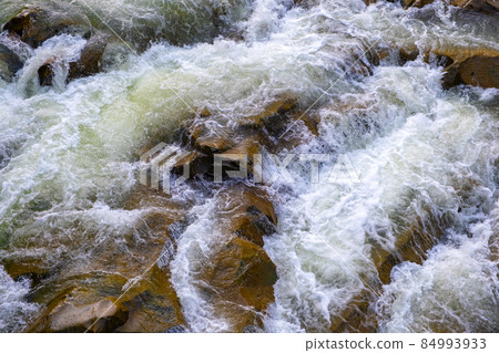 Aerial view of river waterfall with clear turquoise water falling down between wet boulders with thick white foam. 84993933