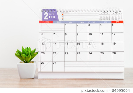 February 2022 desk calendar on wooden table. 84995004