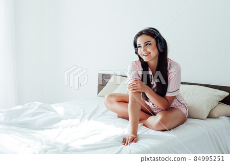 brunette woman in pink pajamas listens to music with headphones 84995251
