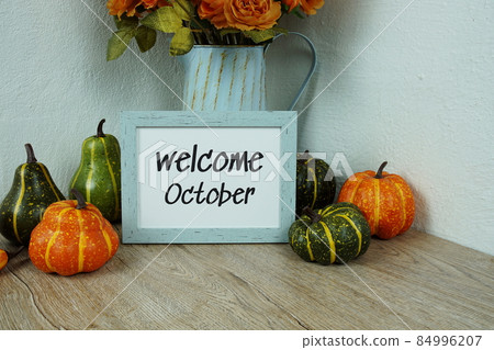 Welcome October typography text with pumpkin decoration on wooden table and white wall background 84996207
