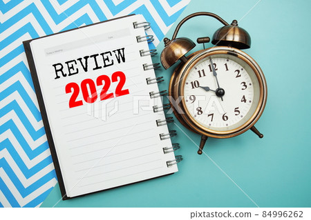 Review 2022 text on paper notebook with alarm clock top view on blue background 84996262