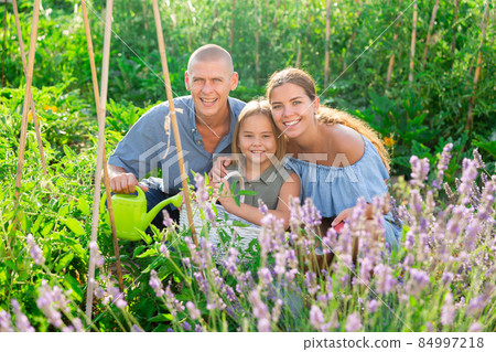 Portrait of daughter and parents with watering cans in summer garden Portrait of daughter and parents with watering cans in summer garden 84997218
