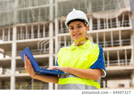 Young woman engineer holds a laptop in her hands, watching the construction process 84997327