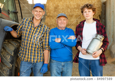 Successful elderly dairy farm owner with adult son and teen grandson standing in hayloft Successful elderly dairy farm owner with adult son and teen grandson standing in hayloft 84997389