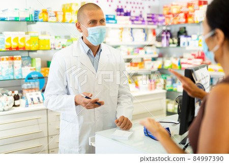 Portrait of pharmacist in medical mask working at the cash register in pharmacy Portrait of pharmacist in medical mask working at the cash register in pharmacy 84997390