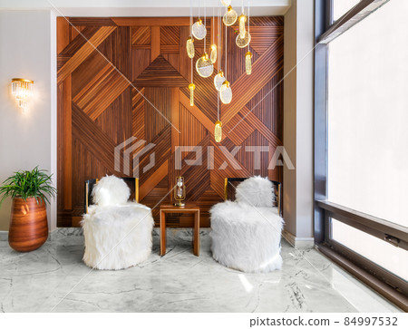 Two modern white feather armless chairs, small wooden modern table, plant pot, and decorated wood cladding wall 84997532