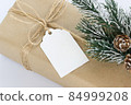 Christmas and New Years background close-up. Gift box wrapped in kraft paper with jute cord. Decorated with a label and a branch with cones 84999208