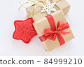 Christmas and New Years decorated gifts. Gift box wrapped in kraft paper with red ribbon. Red knitted heart. Box with jute cord and crocheted snowflake 84999210