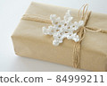 Christmas and New Year background. Gift box wrapped in kraft paper with jute cord. Decorated with a crocheted snowflake 84999211