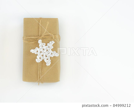 Christmas and New Years flatlay background. Gift box wrapped in kraft paper with jute cord. Decorated with a crocheted snowflake. Place for your text 84999212