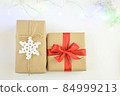 Christmas and New Year background with garland. Gift box wrapped in kraft paper with jute cord. Decorated with a crocheted snowflake. Box with a red ribbon 84999213