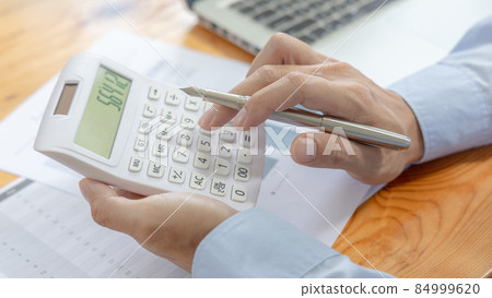 Businessman presses a calculator to calculate earnings and analyze company earnings in his private office, Information in finance and accounting, Company performance and revenue. Businessman presses a calculator to calculate earnings and analyze company earnings in his private office, Information in finance and accounting, Company performance and revenue. 84999620