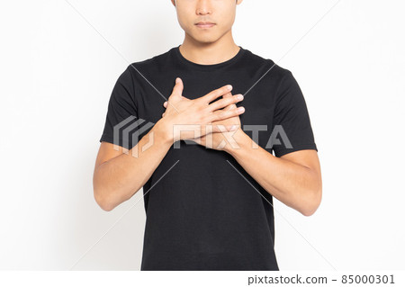 A man wearing a black T-shirt standing in front of a white background and putting his hand on his chest 85000301