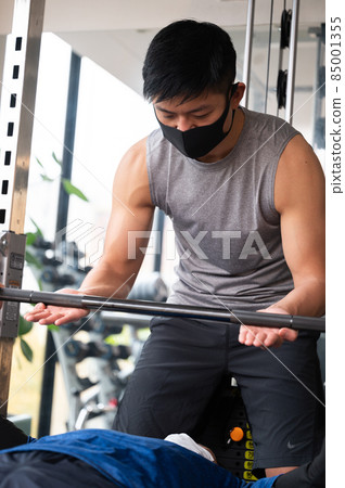 A trainer who teaches muscle training and a person who takes a private lesson with a barbell. 85001355