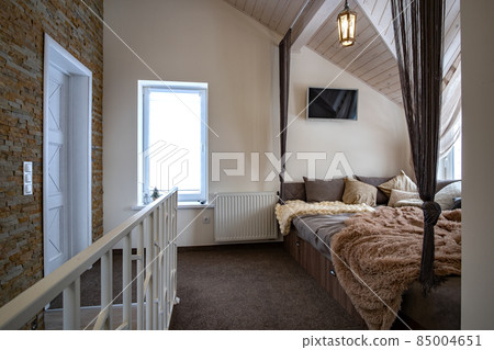 Interior of a modern house spacious hallway with big soft resting place. Contemporary wide sofa with many pillows and light window onder wooden loft ceiling. Interior of a modern house spacious hallway with big soft resting place. Contemporary wide sofa with many pillows and light window onder wooden loft ceiling. 85004651
