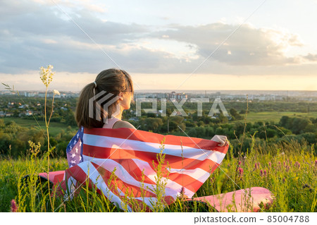 Happy young woman posing with USA national flag standing outdoors at sunset. Positive girl celebrating United States independence day. International day of democracy concept. 85004788
