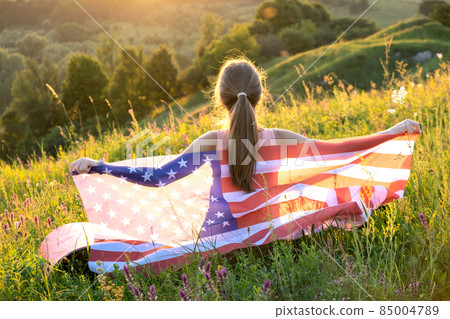 Happy young woman posing with USA national flag standing outdoors at sunset. Positive girl celebrating United States independence day. International day of democracy concept. 85004789