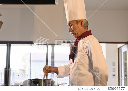 A senior man dressed in cook clothes cooks in the kitchen of a restaurant 85006277