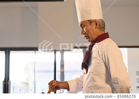 A senior man dressed in cook clothes cooks in the kitchen of a restaurant 85006278