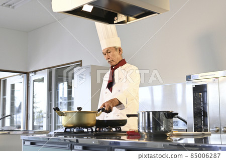 A senior man dressed in cook clothes cooks in the kitchen of a restaurant A senior man dressed in cook clothes cooks in the kitchen of a restaurant 85006287